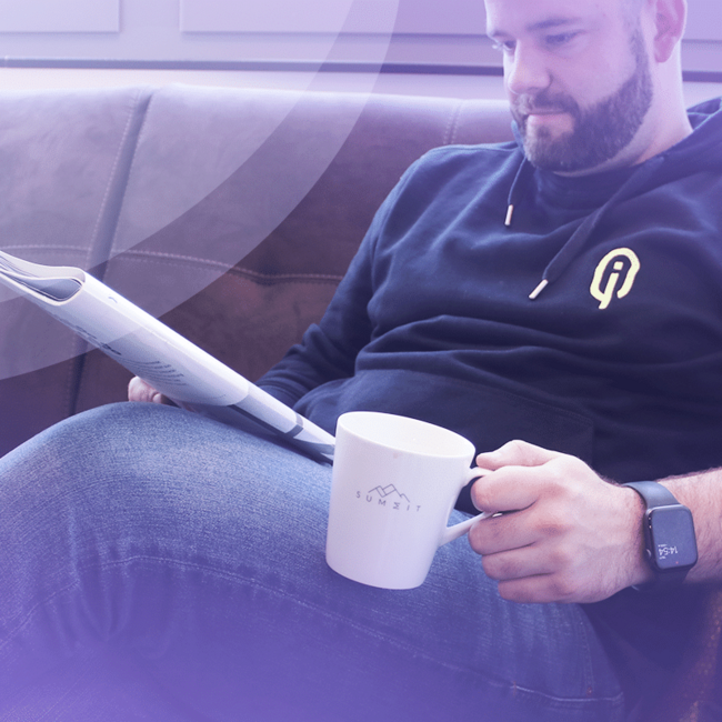 Dieses Bild zeigt Martin im NEUROLOGIQ Hoody, wie er gemütlich eine Zeitung liest und dabei Kaffee aus einer Tasse mit dem Logo von SUMMIT darauf trinkt. Das Titelbild von der Presse-Seite.